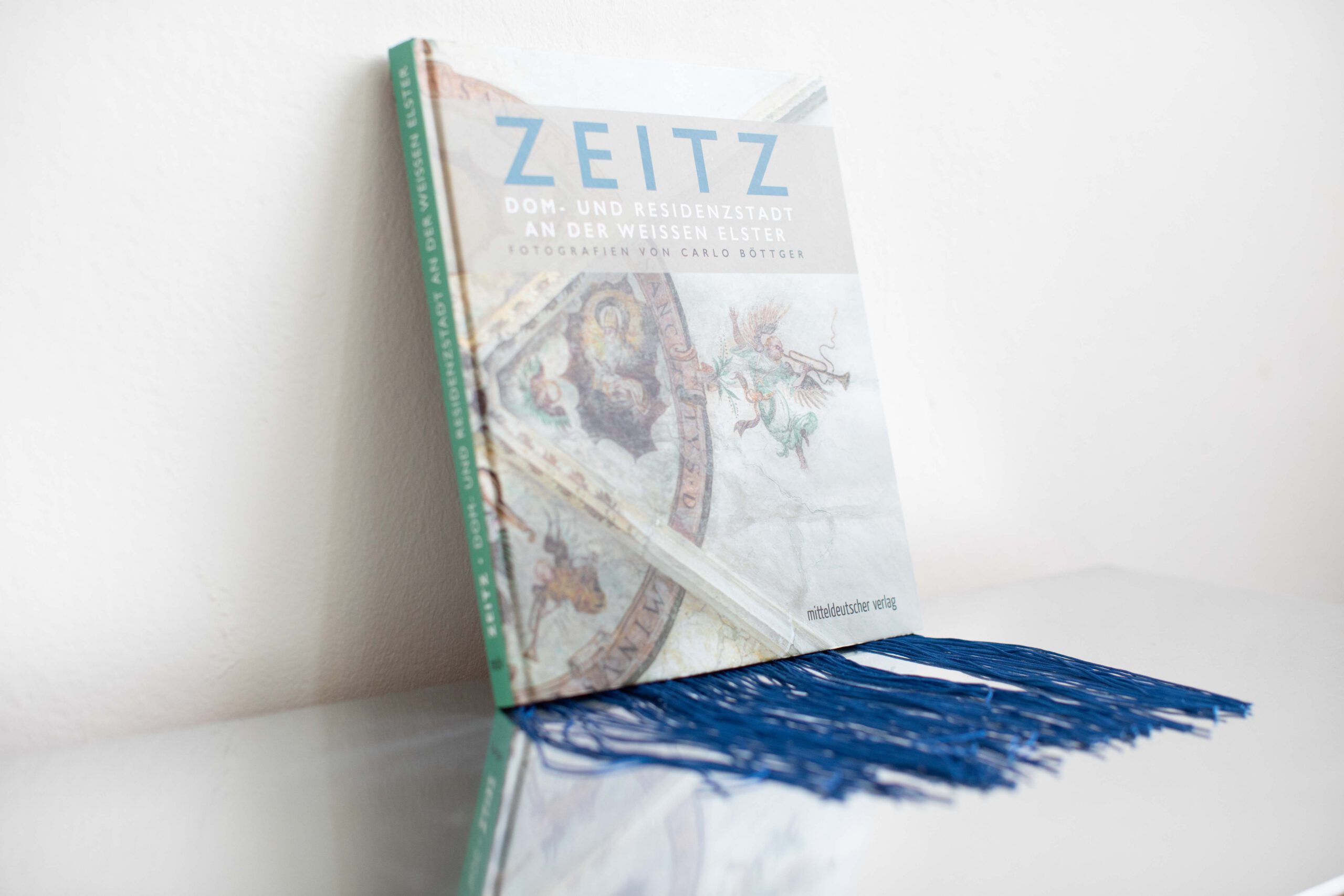 Zeitz-Buch mit blauen Stoff-Fransen auf spiegelnder Oberfläche