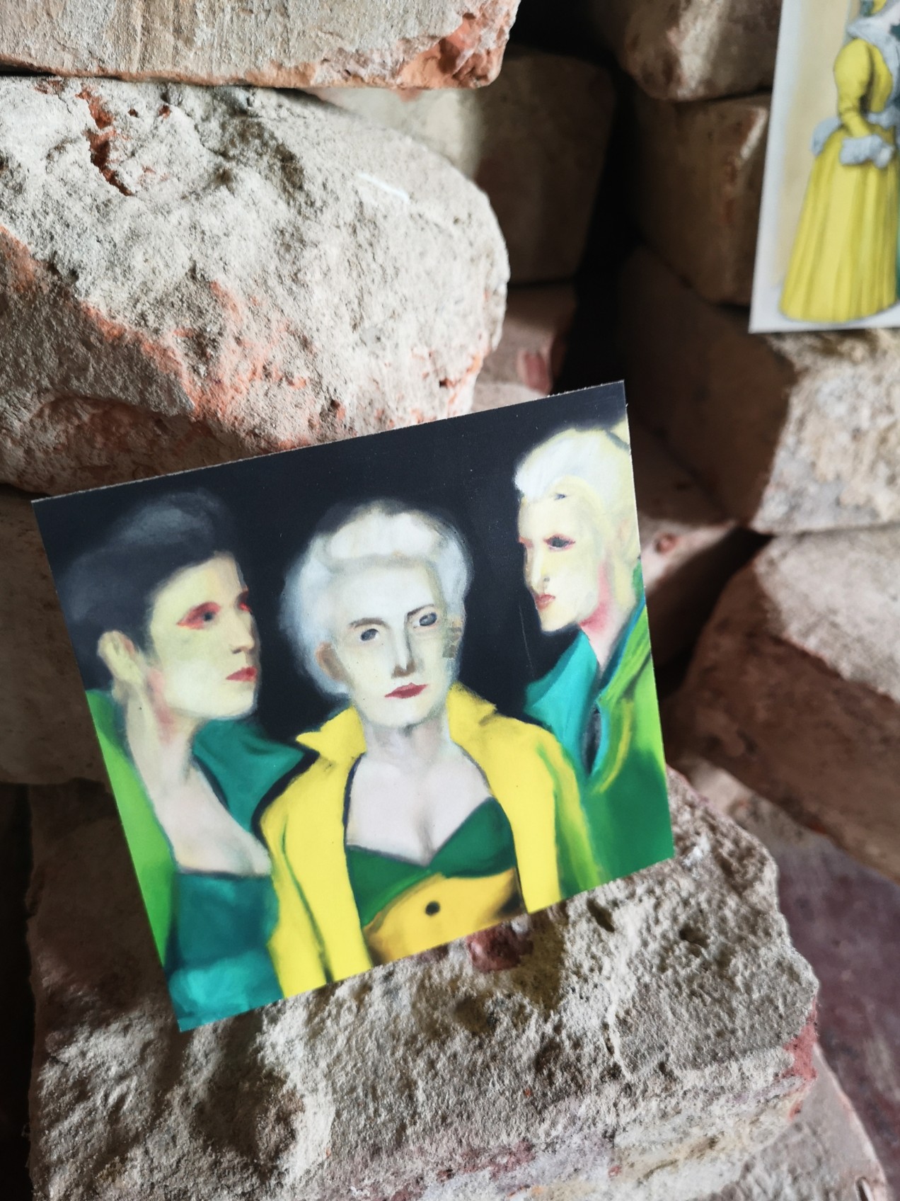 Squared image of three green and yellow dressed women with stones in background.