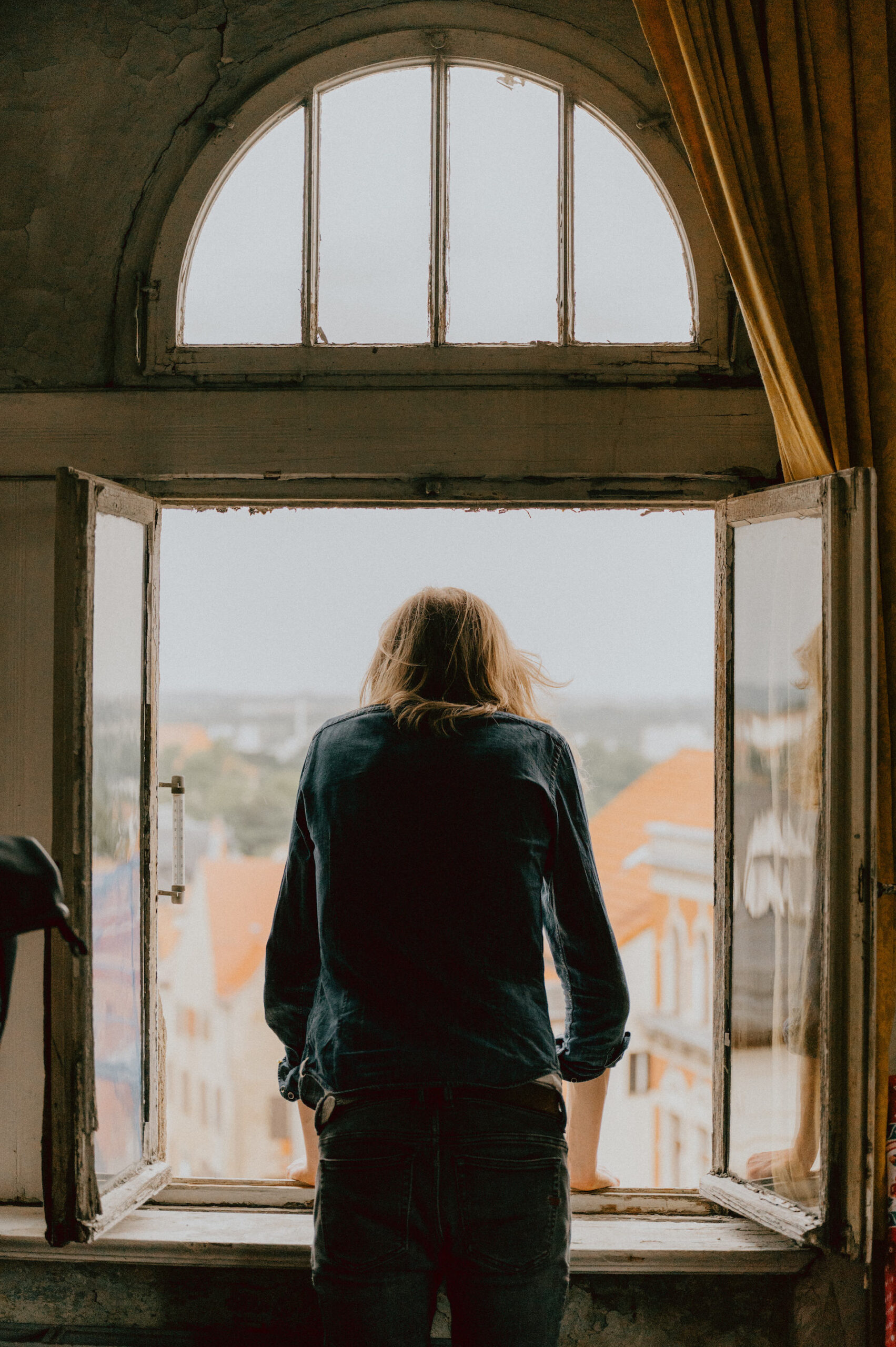 Rückenansicht eines Mannes, der in leer stehendem Gebäude aus dem Fenster schaut