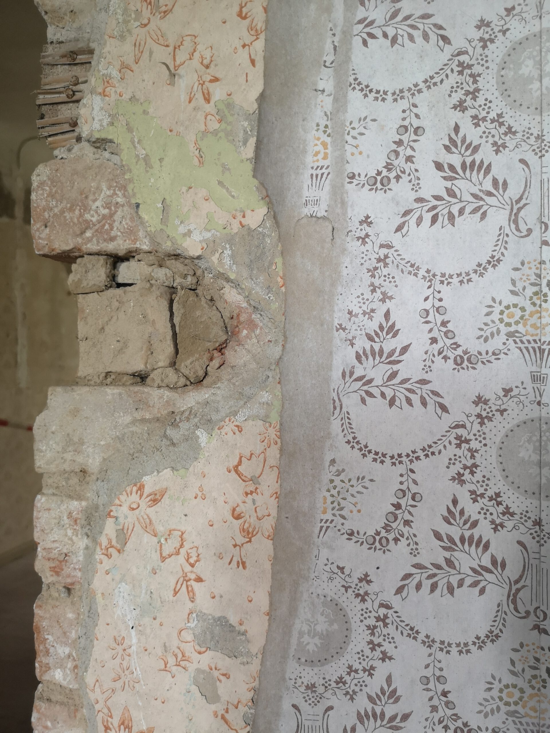 Schichten alter Mustertapeten und Backsteinwand in historischem Gemäuer